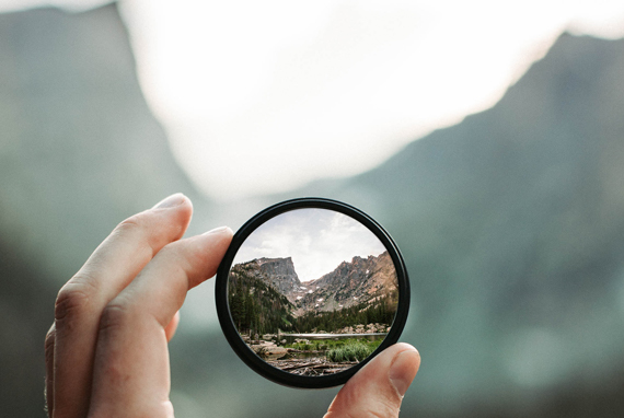 Find Clarity - Image of magnifier pointed towards blurry mountains in the distance, mountains in magnifier is clear.
