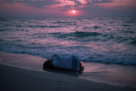 Grief and Loss - Woman laying on beach in fetal position by the waterline, back to camera