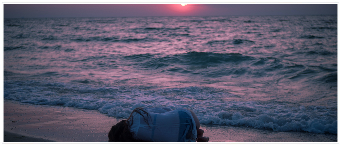 Grief and Loss - Hero Image - Woman laying in fetal position at the beach on the shoreline at sunset.